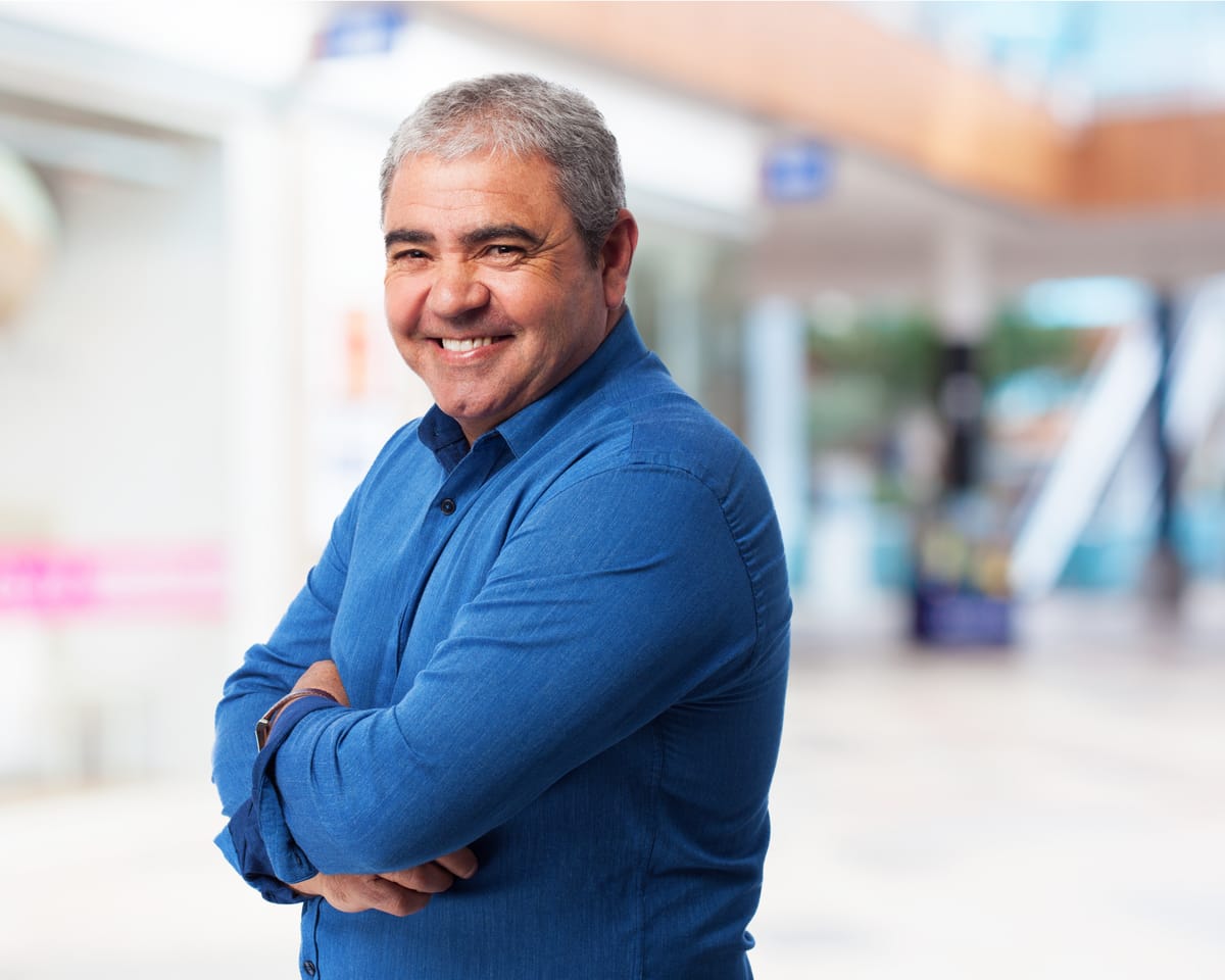 Servidor público sorrindo, de blusa azul, de braços cruzados